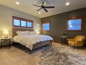 A bedroom with a bed, two bedside tables, a chair, a rug, and a ceiling fan.