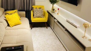 A modern bedroom with a bed, a yellow armchair, a TV, and a window with curtains. - LOCAR-IN GRAMADO- Conte (Gramado)