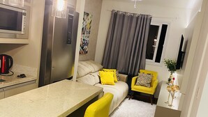 A compact living space with a kitchenette, a dining area with yellow chairs, a bed with a gray headboard, and a small seating area with a yellow chair. - LOCAR-IN GRAMADO- Conte (Gramado)