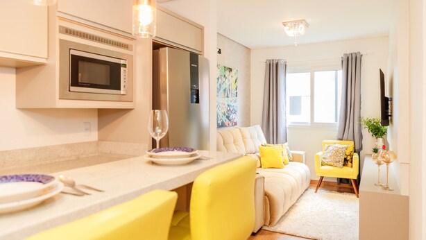 A modern kitchen with built-in appliances, a dining area with yellow chairs, a sofa, and a small yellow armchair. - LOCAR-IN GRAMADO- Conte (Gramado)