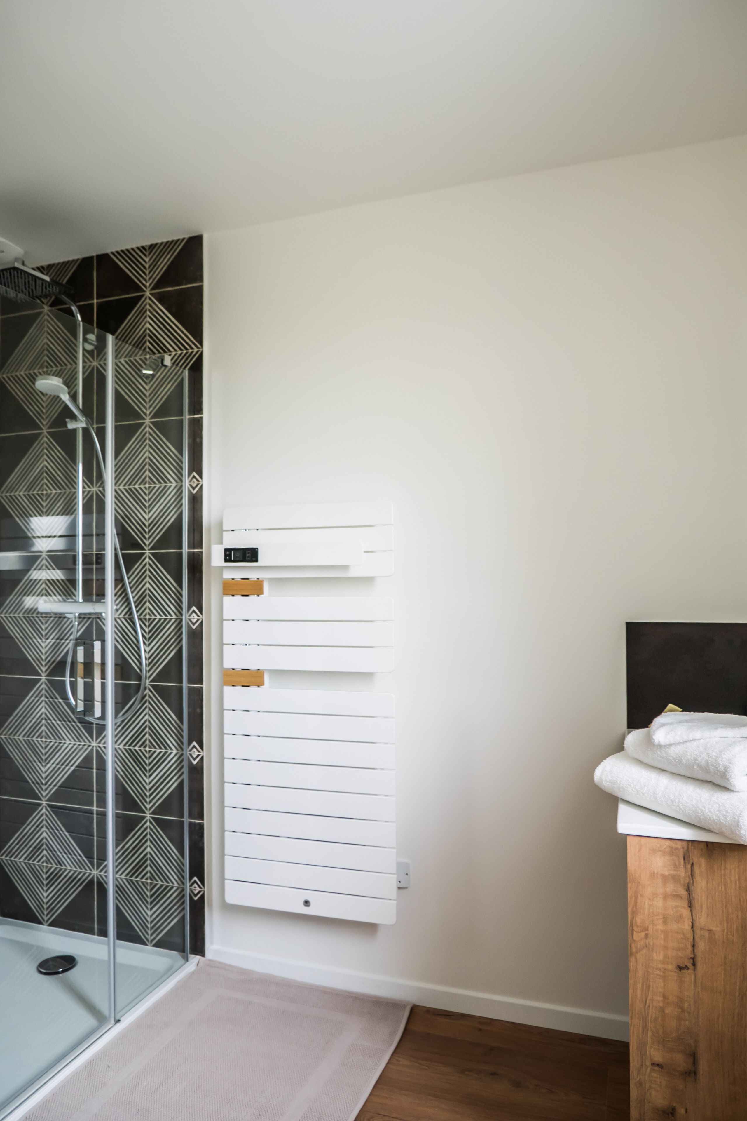 Un baño con cabina de ducha de vidrio, toallero blanco y cabecera de madera.