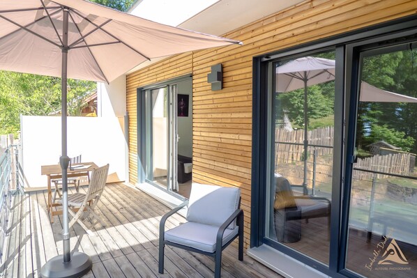 Eine Holzterrasse mit Tisch und Stühlen, einem großen Sonnenschirm und einer Glastür, die zu einem Außenbereich führt.