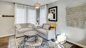 Un salon avec deux canapés, une table basse, une lampe et une décoration murale en macramé.