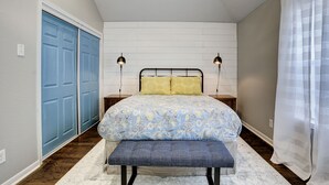 Une chambre à coucher avec un lit, un banc, deux lampes de chevet, une porte bleue et un rideau blanc.