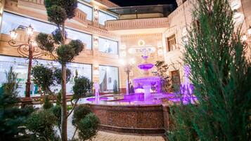 Un hotel de varios pisos con una fuente central, rodeado de jardines bien cuidados e iluminado con una luz ambiental.
