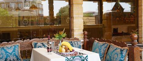 A dining area with a table set for two, featuring a decorative table runner, a fruit bowl, and wine glasses.