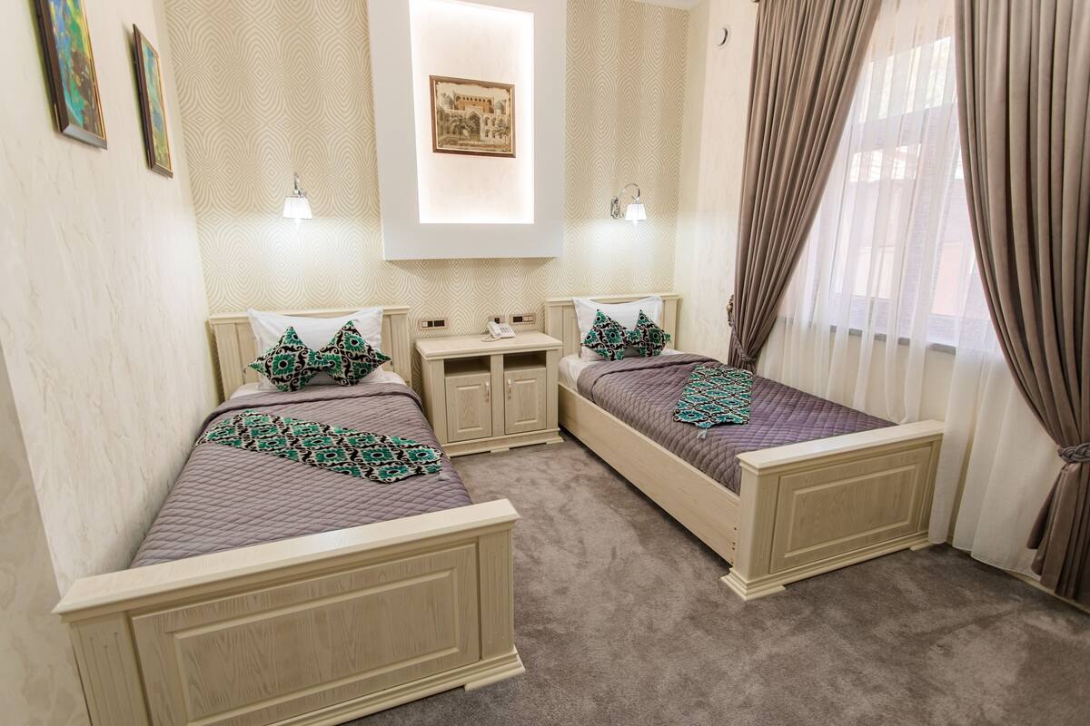 A bedroom with two beds, a bedside table, a nightstand, and a wall-mounted lamp.