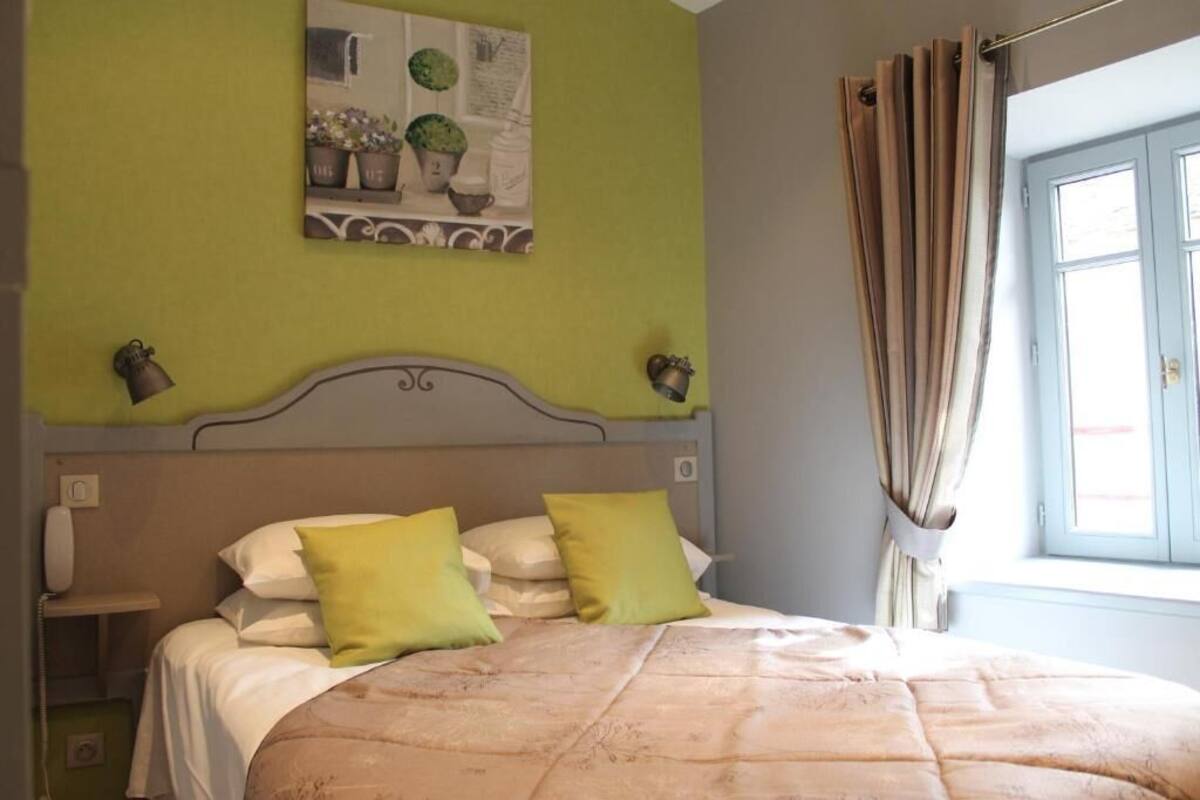 Un dormitorio con cama, mesita de noche, teléfono y ventana con cortinas.