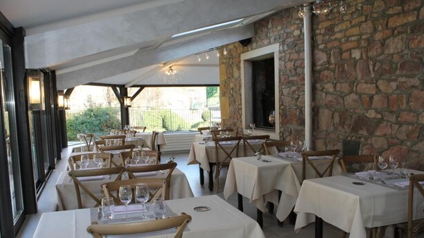 A restaurant with multiple tables and chairs, stone walls, and a view of greenery outside. - Logis Moulin De Saint Verand (Saint-Verand)