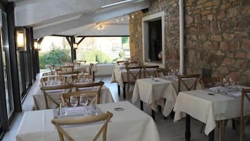 A restaurant with multiple tables and chairs, stone walls, and a view of greenery outside.