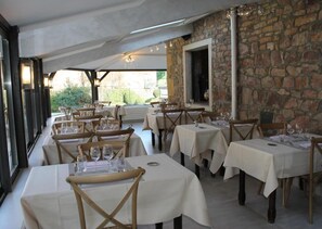 Un restaurante con varias mesas y sillas, paredes de piedra y vistas al exterior a zonas verdes.