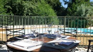 A round wooden table set for dining with a view of a swimming pool and trees in the background.