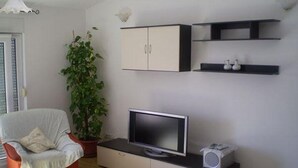A modern living room with a flat-screen TV, a small speaker, a potted plant, and a chair. - Apartment in Duće with Seaview, Balcony, Air condition, WIFI (5060-1) (Duce)