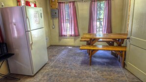 A compact kitchen with a refrigerator, a wooden bench, and a window with curtains. - Zubers - CA -A Cabin A (Concan)
