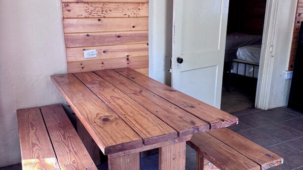 A wooden picnic table with benches, a white door, and a tiled floor. - Zubers - CA -A Cabin A (Concan)