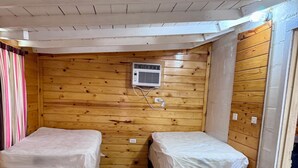 A room with two single beds, wooden walls, a ceiling fan, and an air conditioning unit. - Zubers - CA -A Cabin A (Concan)