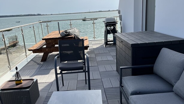 Una terrazza con vista sul mare, con un tavolo in legno, un barbecue e un divano.