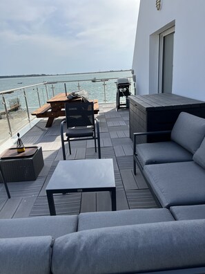 A terrace with a view of the sea, featuring a wooden table, a barbecue grill, and a sofa. - Quiet 130 m2 house with a view of the ocean (PLOUHARNEL)