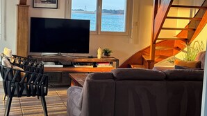 Un soggiorno con una grande televisione a schermo piatto, un divano, una poltrona, un tavolino in legno e una scala.