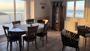 Un'area pranzo con tavolo e sedie, un pensile con vetri e vista sul mare attraverso ampie finestre.