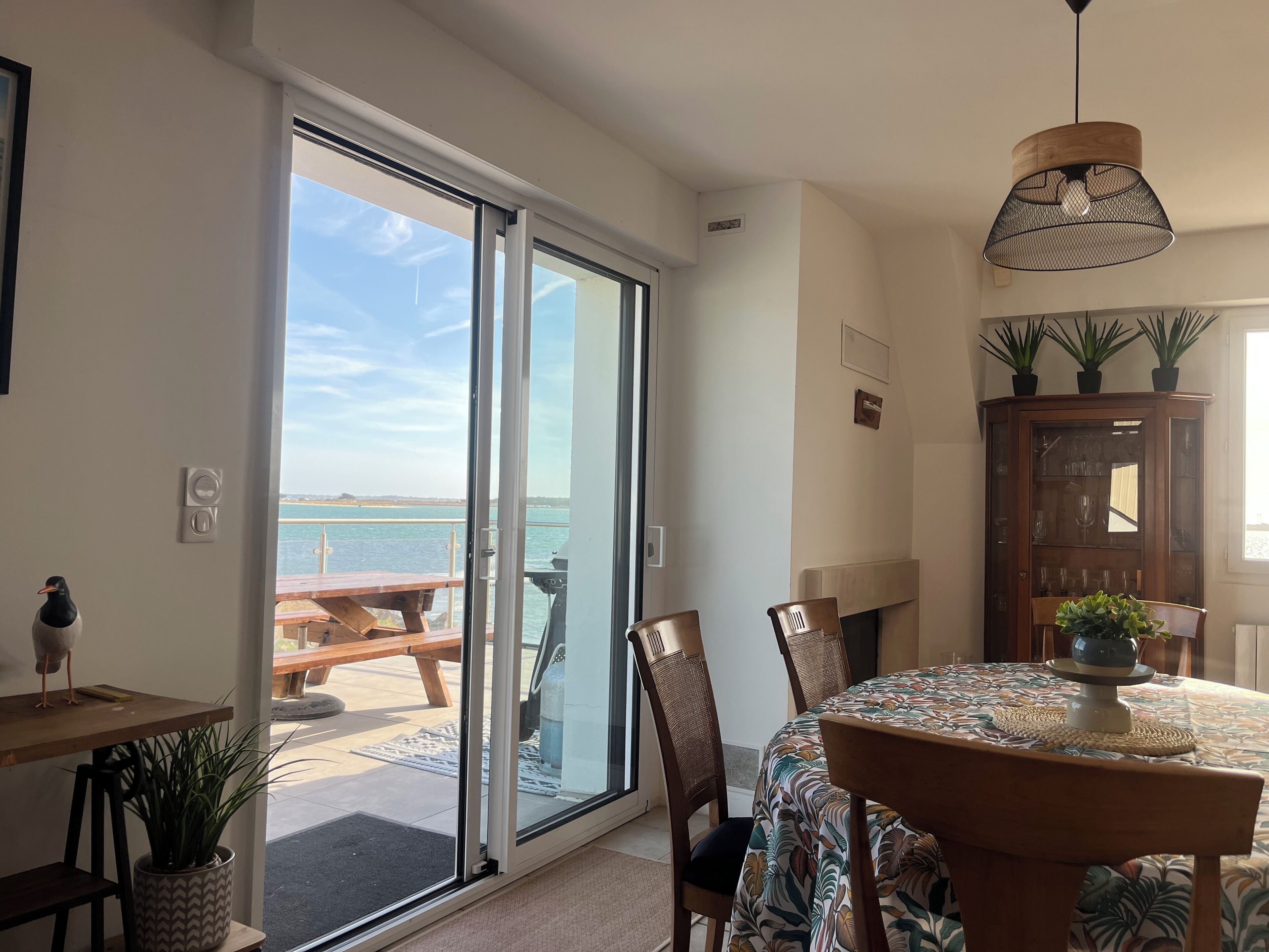A dining area with a table, chairs, and a view of the sea through a sliding glass door.