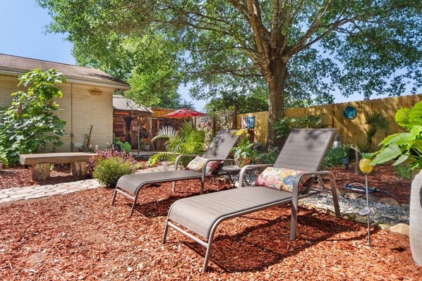 A patio area with metal lounge chairs, a stone bench, and a wooden fence. - Sleeps 6 with Garden/Bar (Milton)