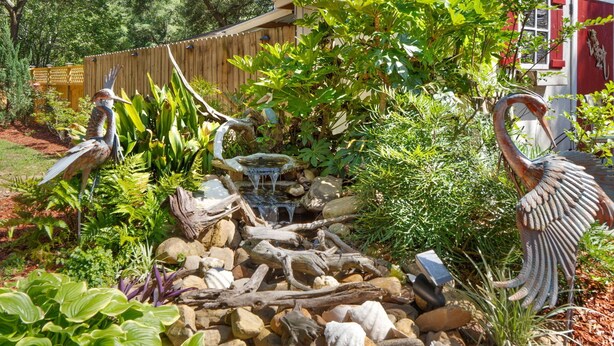 Un jardin agrémenté d’un bassin, de rochers et de sculptures d’oiseaux.