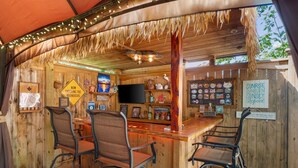Un coin bar rustique avec des murs en bois, un toit de chaume et un comptoir avec des tabourets.
