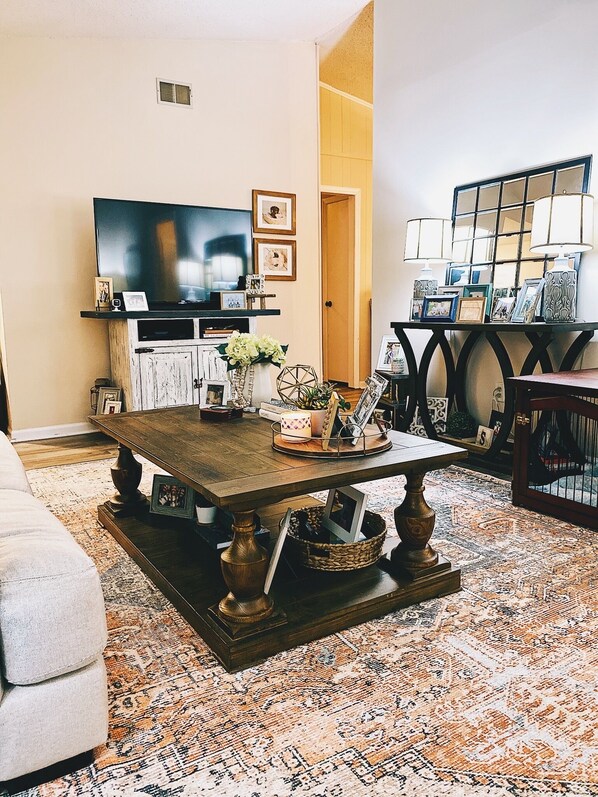A living room with a large flat-screen TV, a wooden coffee table, and a patterned rug.