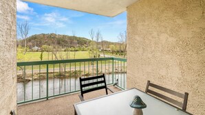 Een balkon met uitzicht op een rivier en een groene hekken. Er staat een tafel met een stoel en een decoratief object op.
