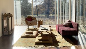 A modern living room with large windows, a wooden coffee table, a red sofa, and a patterned rug. - Modern Glass House designed by renowned architect Thomas Phifer (Hudson)