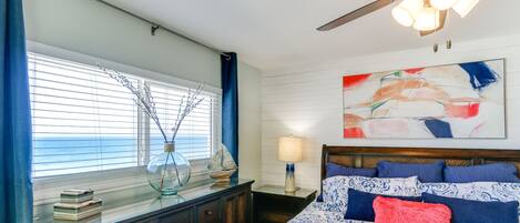 Un dormitorio con una cama grande, un ventilador de techo, una ventana con persianas, un aparador y un cuadro en la pared.