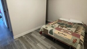Ein Schlafzimmer mit einem Bett, das mit einer geblümten Stegdecke bezogen ist, Holzdielen und einer schrägen Decke.