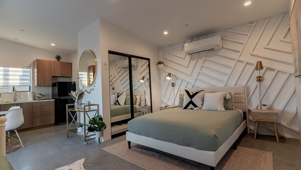 A modern bedroom with a large bed, bedside tables, a desk, and a kitchen area with cabinets and a refrigerator. - 15%DISCOUNT❤Hammocks❤Close 2 Downtown❤Fully Fenced (Joshua Tree)
