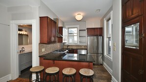 A modern kitchen with a central island, stainless steel appliances, and wooden bar stools. - Breathtaking Spacious PGH Skyline Loft On Carson Street (Pittsburgh)