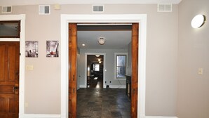 A hallway with a wooden floor, white walls, and a door leading to another room. There are two wall-mounted light fixtures and a ceiling vent. - Breathtaking Spacious PGH Skyline Loft On Carson Street (Pittsburgh)