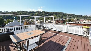A wooden deck with a table and benches, white railings, and a view of a town with buildings and hills in the background. - Breathtaking Spacious PGH Skyline Loft On Carson Street (Pittsburgh)