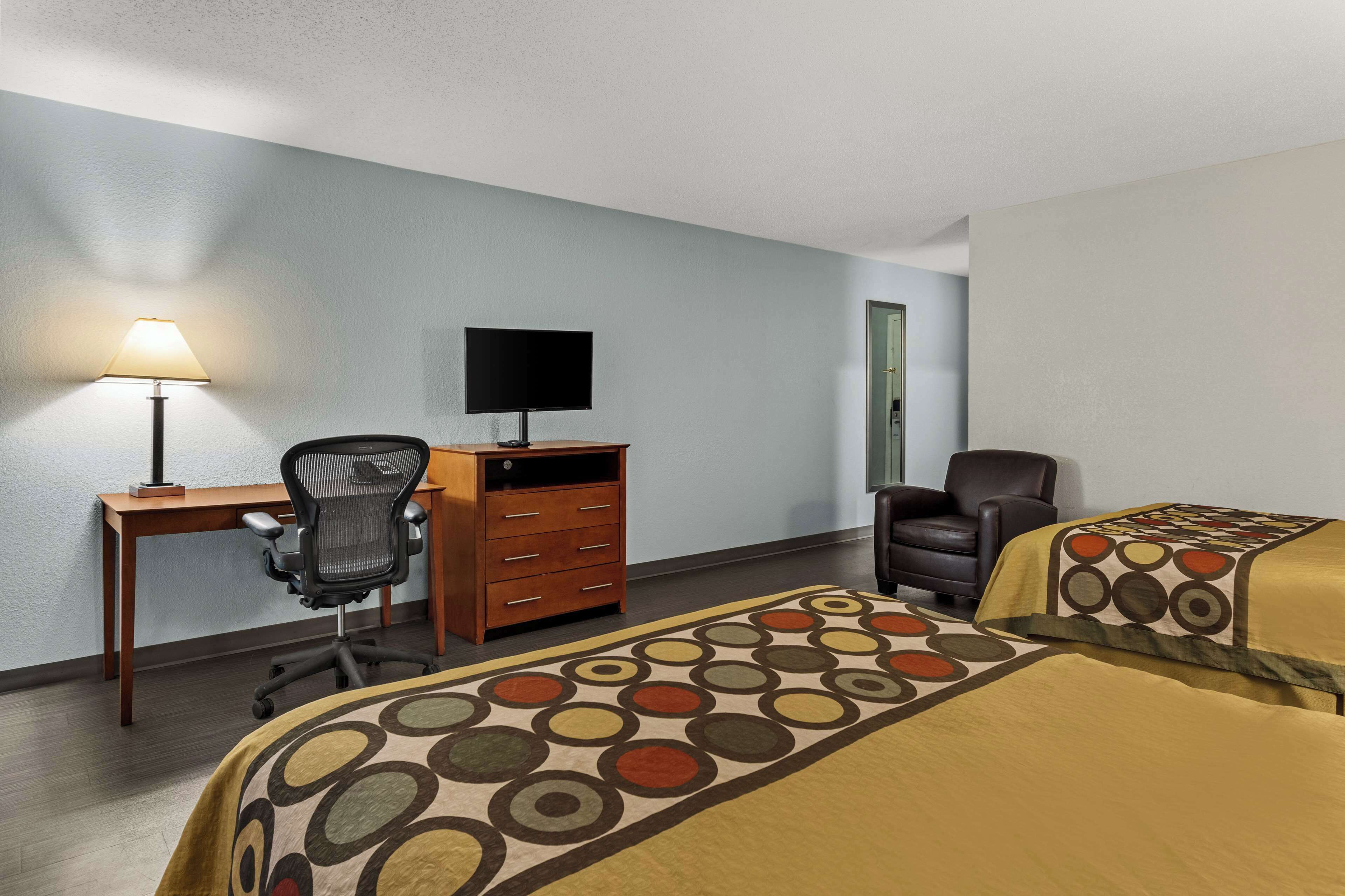 Habitación de hotel con dos camas, un escritorio con computadora, una silla y una lámpara.
