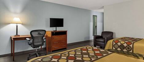 Habitación de hotel con dos camas, un escritorio con computadora, una silla y una lámpara.