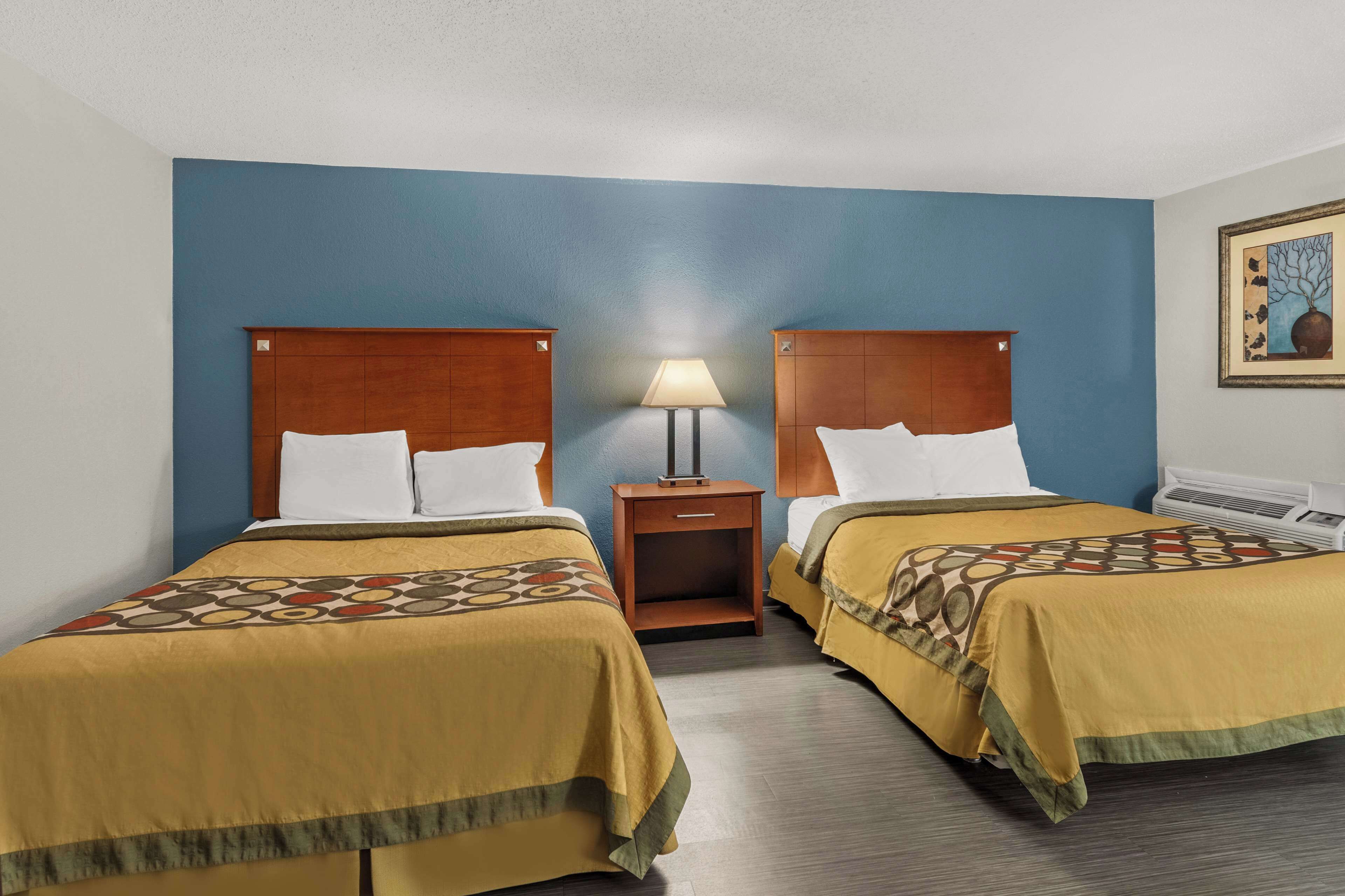 A hotel room with two beds, a nightstand with a lamp, and a painting on the wall.
