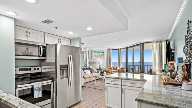 A modern kitchen with stainless steel appliances, a dining area with a view of the ocean, and a living room with a large window overlooking the sea. - Sunbird 1103 West (Panama City Beach)