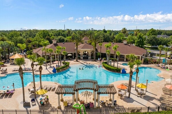 A resort with a large central pool, palm trees, and a covered area with seating.