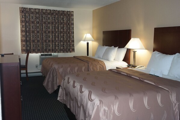 A hotel room with two beds, a desk, a chair, a lamp, and a patterned curtain. - Quality Inn in Janesville, WI (Janesville)