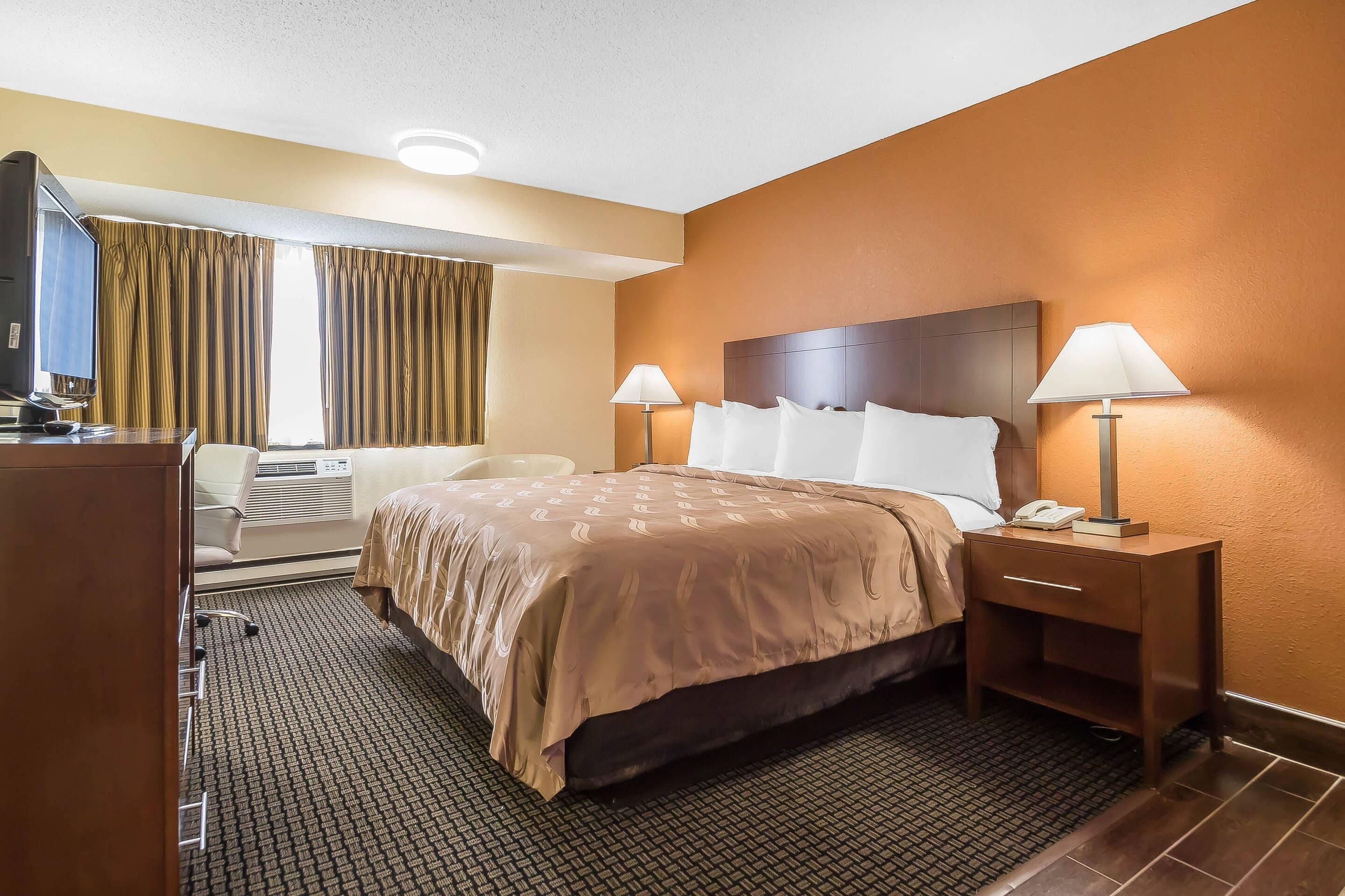 A hotel room with a bed, two bedside lamps, a desk with a telephone, and a television.