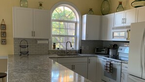 A kitchen with white cabinets, a granite countertop, a window with a view of trees, and a microwave.
