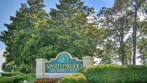 A sign for Myrtlewood Golf Resort & Villas with a landscaped foreground and trees in the background.