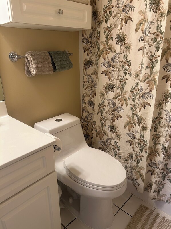 A bathroom with a toilet, a towel rack with a folded towel, and a shower curtain with a floral pattern. - Cozy Retreat in Myrtle Beach: On-Site Golf and Pools! Only 1 mile to Beach! (Myrtle Beach)