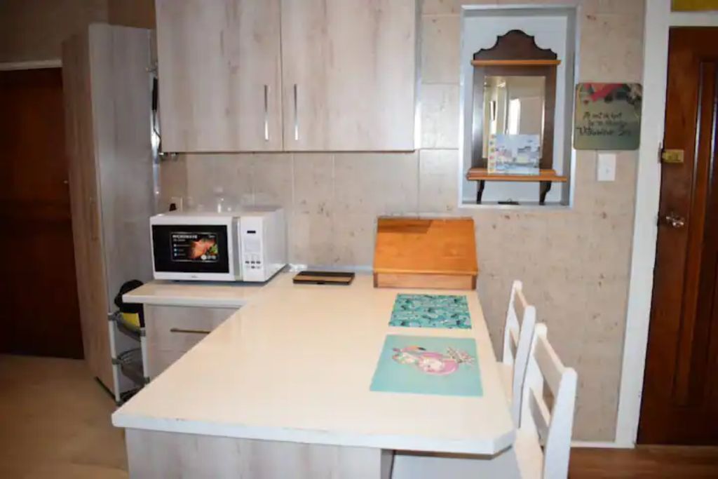 Uma cozinha compacta com micro-ondas, uma mesa de madeira e algumas cadeiras.