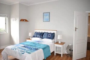 A bedroom with a bed, bedside tables, a nightstand, a wall-mounted shelf, a picture, and a door.