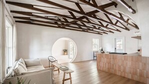 Amplia habitación con techo de madera, ventanal redondo, sofá, mesa de comedor y zona de cocina.